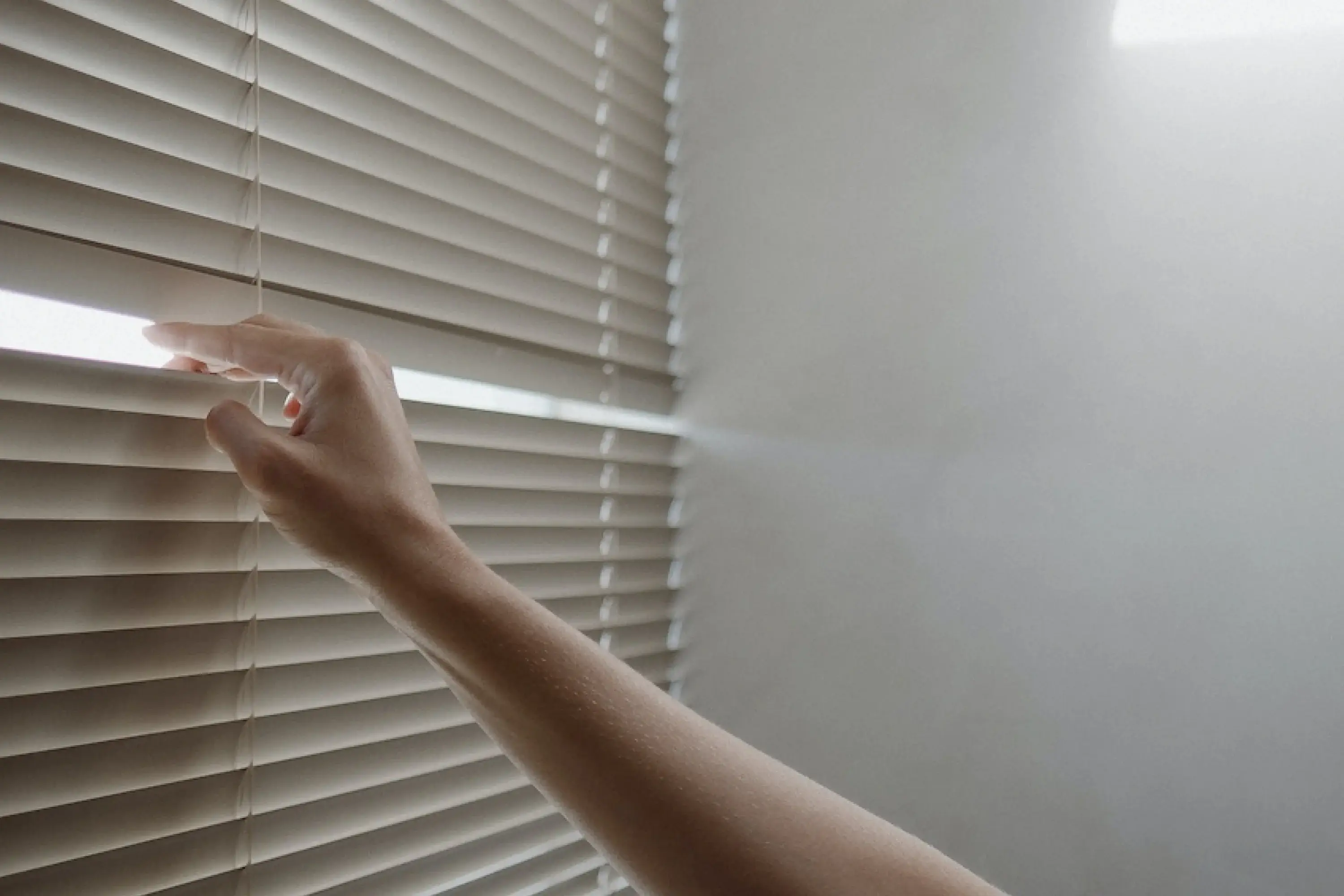 hand peeling through the blinds with sun coming through 